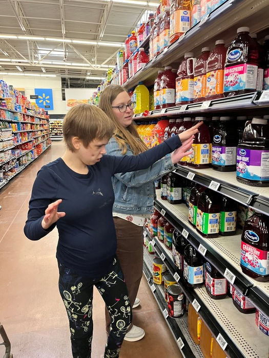 A young woman shopping for juice in the grocery aisle assisted by her teacher