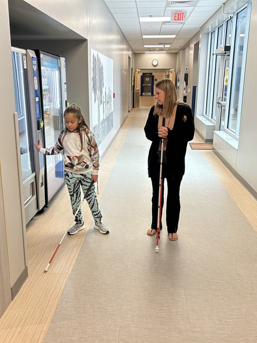A young girl feeling the vending machine in the hallway during an O&M lesson with her teacher