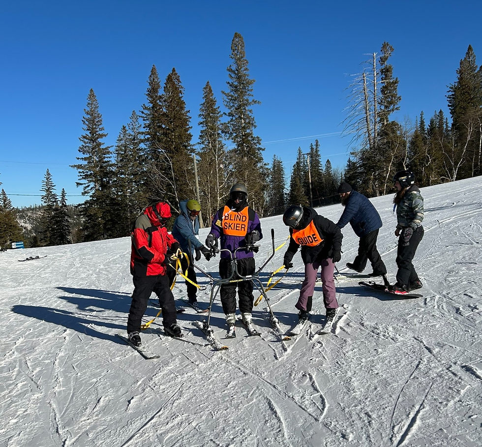 A young man on downhill skis holding onto a slider device for balance, standing with his guides after a fun run down the hill at Ski for Light in Black Hills, SD
