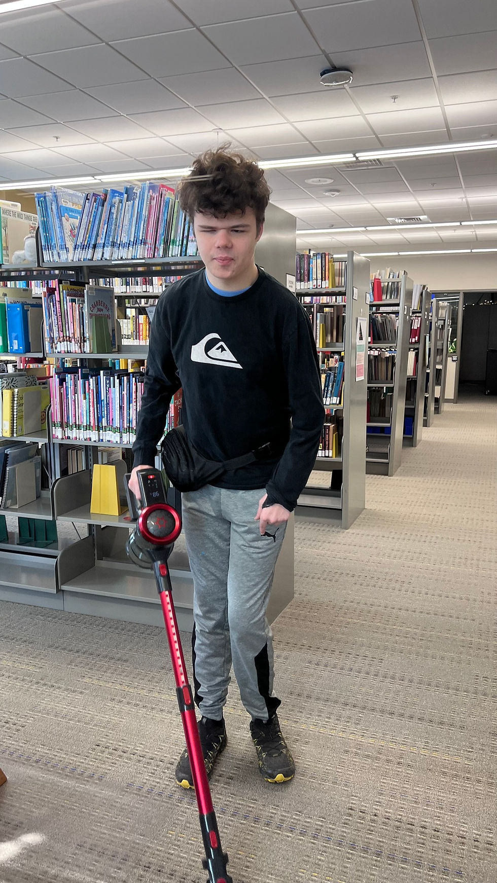 A young man independently vacuums the carpet in the library