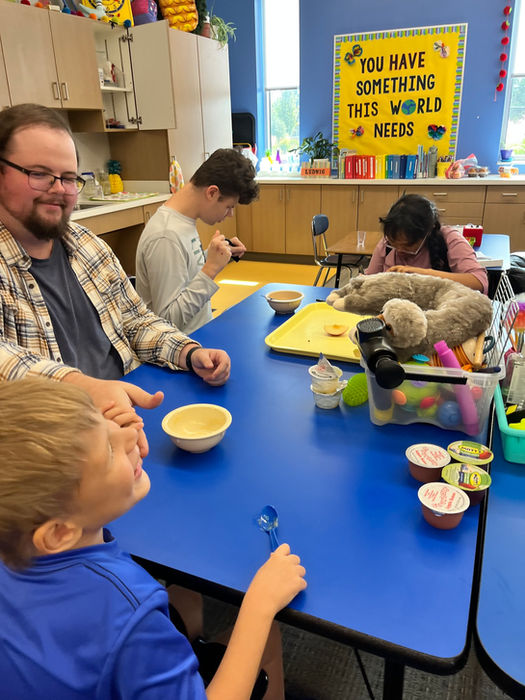 Students gathered around a table with their teacher tasting different flavors of applesauce