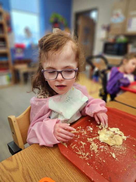 A young girl smiling as her fingers touch the pudding and graham cracker mixture on her tray