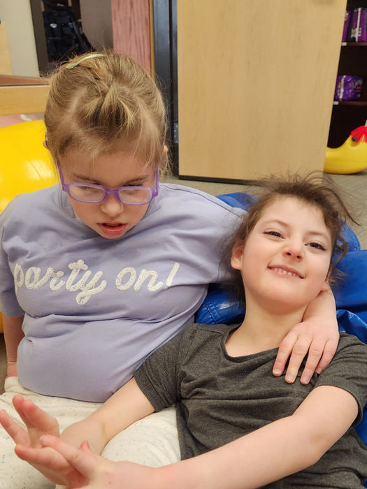 Two young girls enjoying indoor recess on the floor, with one girl having her arm around the other