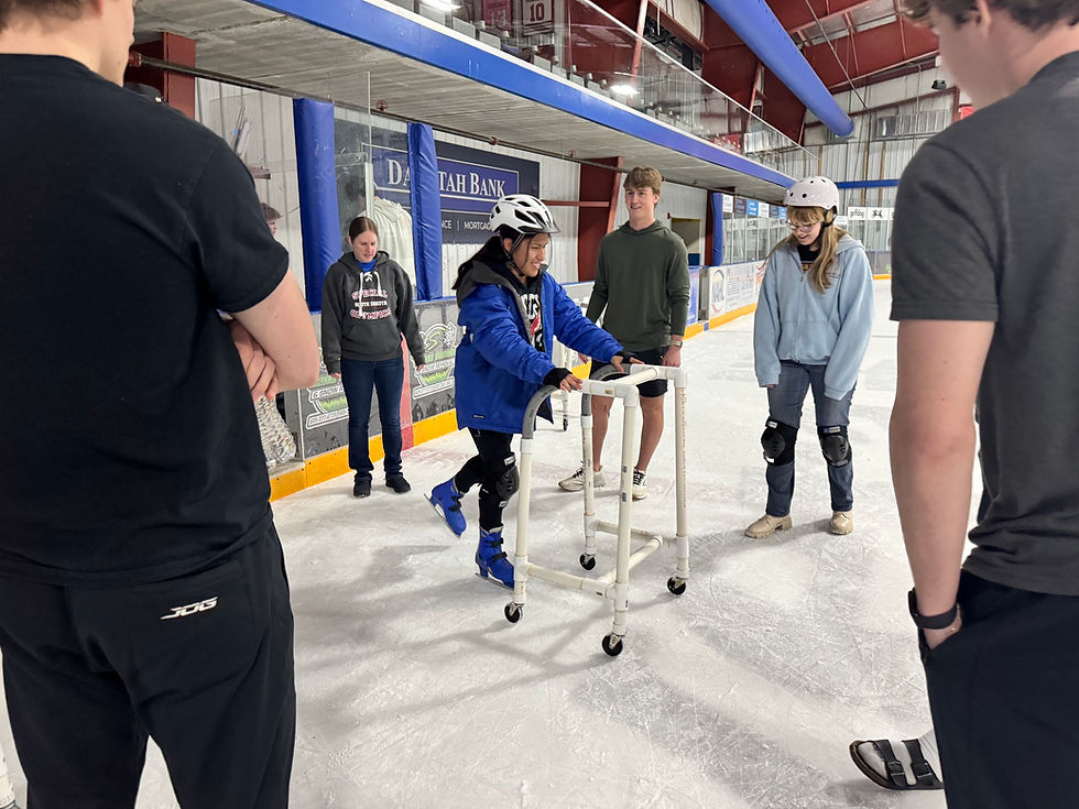 A young woman is ice skating with the aid of a wheeled walker while a crowd of students, a teacher, and Wings hockey players watch