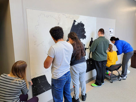 Students working on a tile mural of the school's logo with the assistance of staff.